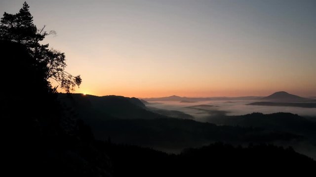 Last moments before autumn daybreak in hilly landscape. Hill peaks increased from orange and pink foggy sea. Time lapse 