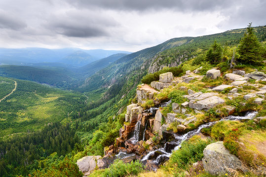 Fototapeta Beautiful waterfall above a deep green valley with mountains