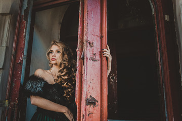 Beautiful girl in green vintage dress with coat walking near ancient house and door. Vintage farytale concept. Woman with long hair and make up