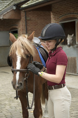Young rider preparing a pony for her riding lesson - September 2016 - Teenager adjusting the bridle