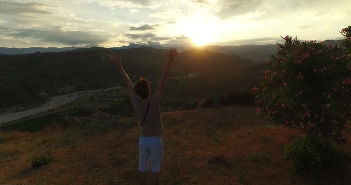 Giovane ragazzo con le mani in aria soddisfatto e spensierato guarda il tramonto alla fine di una giornata.
