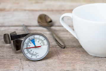 The thermometer for coffee, coffee cups and a spoon placed on a wooden floor.