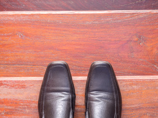 top view Black leather shoes on a wooden ladder. wearing black leather shoes standing on a wooden ladder.
