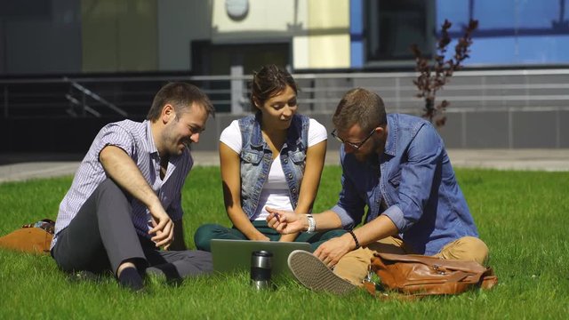 three students sit on the lawn and prepare for lessons