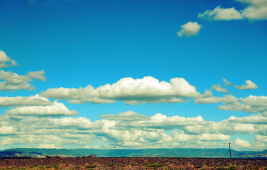 Rural cloudscape with flat road and power lines in foreground and mountain range in background. Retro toned image.