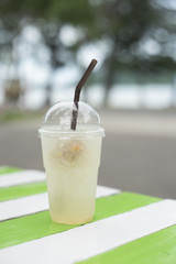iced plum juice in takeaway cup on wooden table,blurred sea in background,selective focus