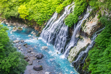 Fototapeta na wymiar Shirogane waterfall with blue stream at Biei, Japan