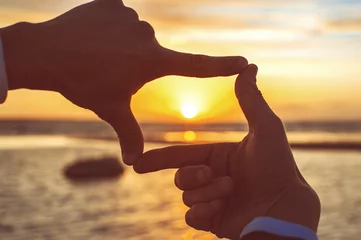 Foto op Plexiglas Samenstelling vingerkader - de handen van de man vangen de zonsondergang © AnnaElizabeth