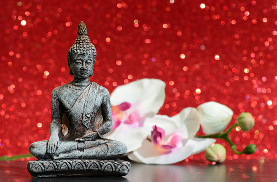 Buddha statue and a orchid flower on a bright red shiny glitter background with bokeh