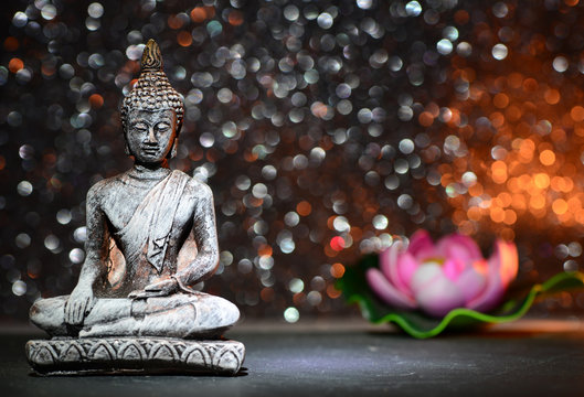 Zen Buddha statue and a lotus flower on a bright shiny glitter background with bokeh