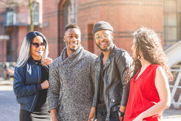 Mixed race group portrait in Hamburg, Germany. Four persons, with different ethnicities and wearing urban style clothes, looking each other and smiling. Lifestyle and friendship concepts.