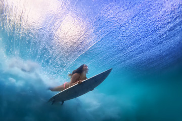 Sportive girl in bikini in action. Surfer with surf board dive underwater under breaking ocean...