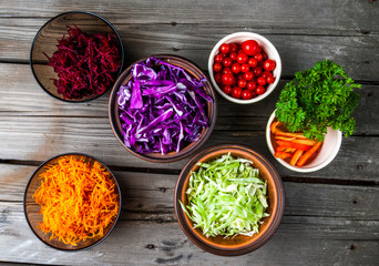 Selection of autumn vegetables, rich in vitamins. Set for cooking fresh salad or vegetable stew. In the glass, ceramic and clay bowls on a wooden table, top view. 