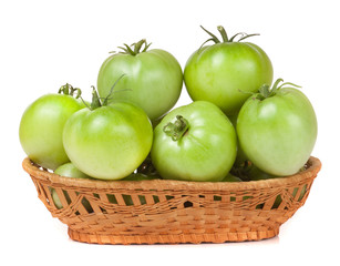 unripe green tomatoes in a wicker basket isolated on white background