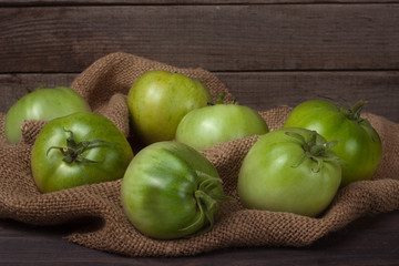 some green unripe tomato on the wooden background with burlap