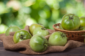 unripe green tomatoes in a wicker basket on wooden table with blurred background