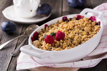 Plum and raspberry crumb on the old wooden background. Rustic style. Selective focus.