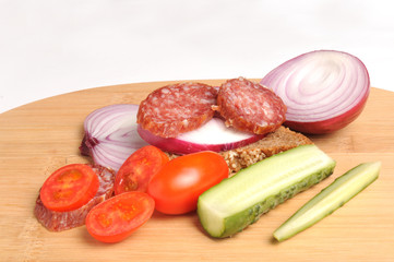 summer sausage , salted cucumber, red cherry tomatoes and sliced red onion Bamboo cutting board , traditional snack while drinking vodka