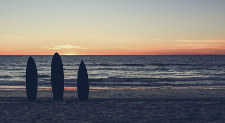 Retro  photo of a  silhouette of surfboards on the  beach at sunset 