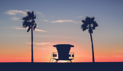 Vintage photo of a silhouette of a  Lifeguard tower on the beach at sunset with palm trees 