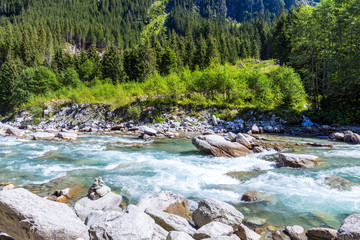 Austrian Alps. Starting famous Krimml waterfalls. Crystal clear water sparkles in the midday sun. Through the narrow creek wooden bridge spanned