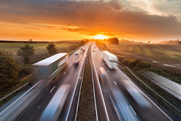 Trucks and Cars in Motion on Busy Motorway at Sunset - obrazy, fototapety, plakaty