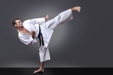 Handsome young black belt male karate doing kick on the gray background