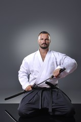 Handsome young black belt male karate posing with sword on the gray background