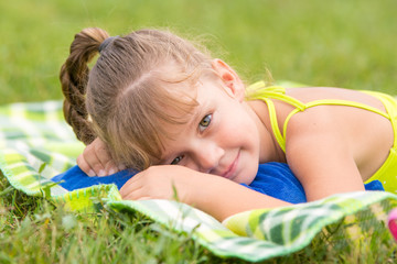 Five-year girl lies on a green meadow and touching looking to the frame