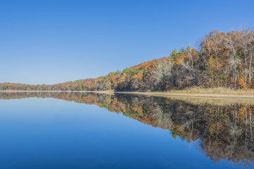 Colorful mirror reflection of rusty autumn colors along a tranquil lake. 