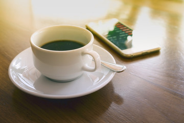 A cup of black coffee in the morning and stock market news, analysis of the market data on smartphone, (With warm sunlight effect created reflection on the table, smartphone)