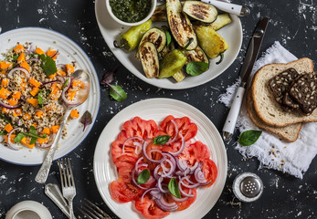 Vegetarian dinner table -  quinoa and pumpkin salad, tomatoes, eggplants and peppers on the grill. On a dark background, top view. Healthy vegetarian diet food
