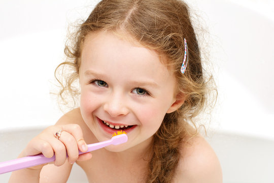 Young girl brushing teeth while sitting in the bath and smiling