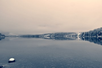 Snowy winter landscape on the lake in black and white, on a cloudy, foggy day. Monochrome image filtered in retro, vintage style with soft focus and red filter. Lake Bohinj, Slovenia - 121695735