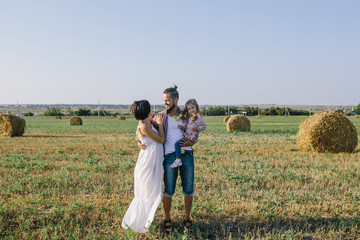 father in a red plaid shirt, daughter and pregnant mother in white dress enjoying life outdoor in field