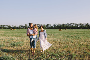 Naklejka na ściany i meble father in a red plaid shirt, daughter and pregnant mother in white dress enjoying life outdoor in field