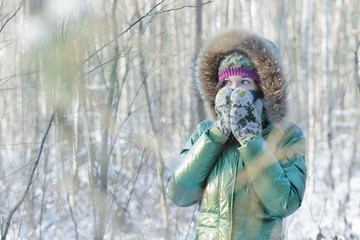 Young woman in winter frost forest hiding her face in woolly scarf and mittens outdoors