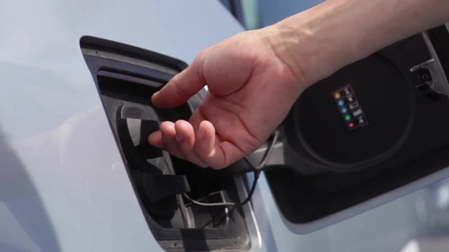 Color footage of a man's hand opening the lid of an electrical car, for charging.