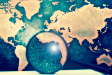 Magnifying lens on books against grunge world map, with lens flare