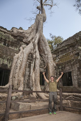 Fototapeta premium Tourist at Ta Prohm temple in Angkor. Majestic spung tree grows throught the ancient walls of the temple