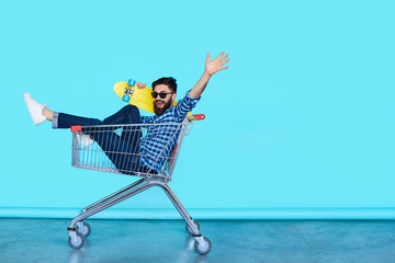 Side view of cheerful young man sitting in shopping cart