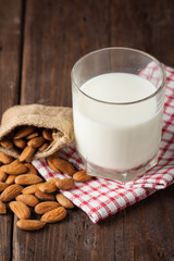 Almond milk in a glass with almond nuts on a wooden table. Healthy food and drink concept.