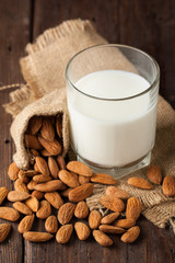 Almond milk in a glass with almond nuts on a wooden table. Healthy food and drink concept.