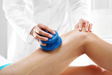 Drenaż limfatyczny.Kosmetyczka masuje uda kobiety gumowymi bańkami do masażu.