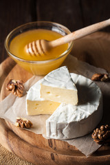 Brie type of cheese. Camembert cheese. Fresh Brie cheese and a slice on a wooden board with nuts, honey and leaves. Italian, French cheese.