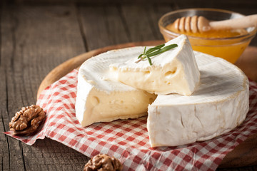 Brie type of cheese. Camembert cheese. Fresh Brie cheese and a slice on a wooden board with nuts, honey and leaves. Italian, French cheese. - obrazy, fototapety, plakaty