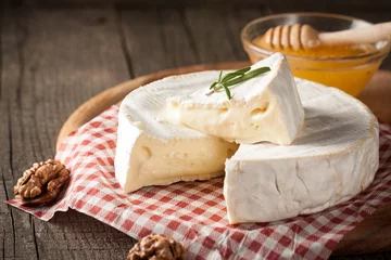 Foto op Plexiglas Brie type of cheese. Camembert cheese. Fresh Brie cheese and a slice on a wooden board with nuts, honey and leaves. Italian, French cheese. © jeny_lk