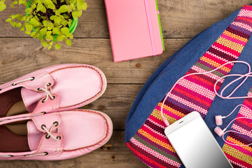 colorful bag, smart phone, headphones, notepad and pink shoes on wooden desk