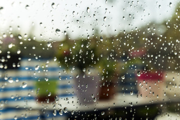 Raindrops after the rain on the window. In background some multicoloured flowers and some blurred city details. 