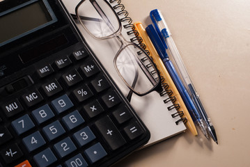 Calculator, glasses and a Notepad on the table, leather notebook,